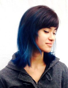 Headshot of woman wearing grey jacket showcasing layered hairstyle with blue ends